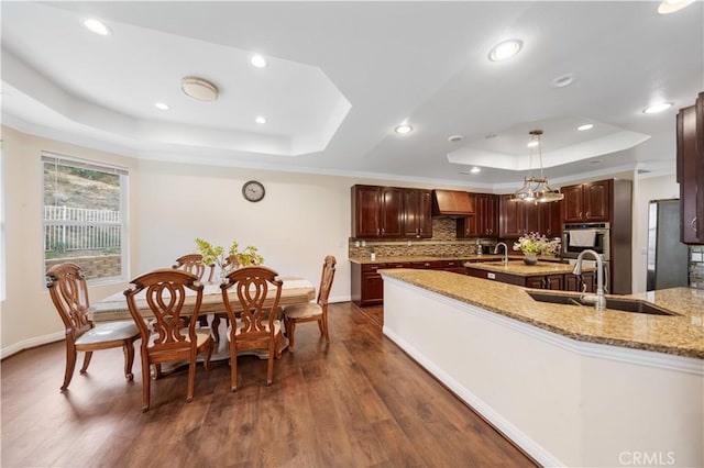 kitchen with a tray ceiling, pendant lighting, custom exhaust hood, a sink, and light stone countertops