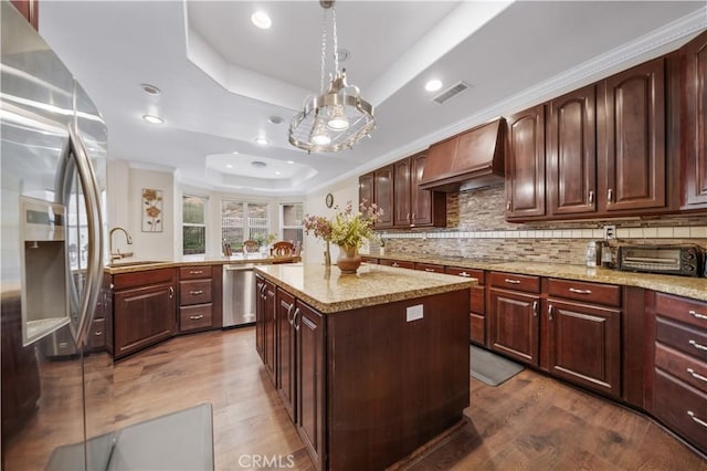 kitchen with stainless steel appliances, visible vents, custom exhaust hood, a tray ceiling, and pendant lighting