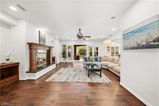 living room featuring dark wood-style flooring, a glass covered fireplace, visible vents, and baseboards