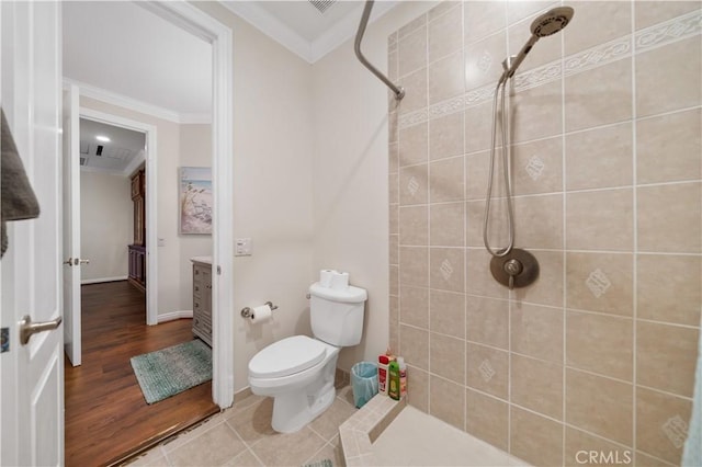 bathroom with tiled shower, toilet, tile patterned floors, crown molding, and vanity