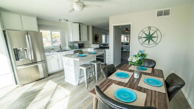 kitchen featuring white cabinetry, stainless steel appliances, a center island, sink, and a kitchen bar