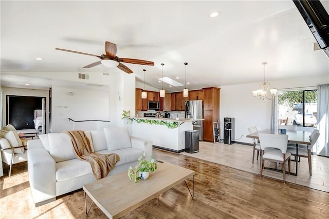 living room with ceiling fan with notable chandelier, light hardwood / wood-style floors, and lofted ceiling