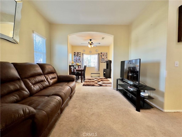 carpeted living room with arched walkways, a ceiling fan, and baseboards