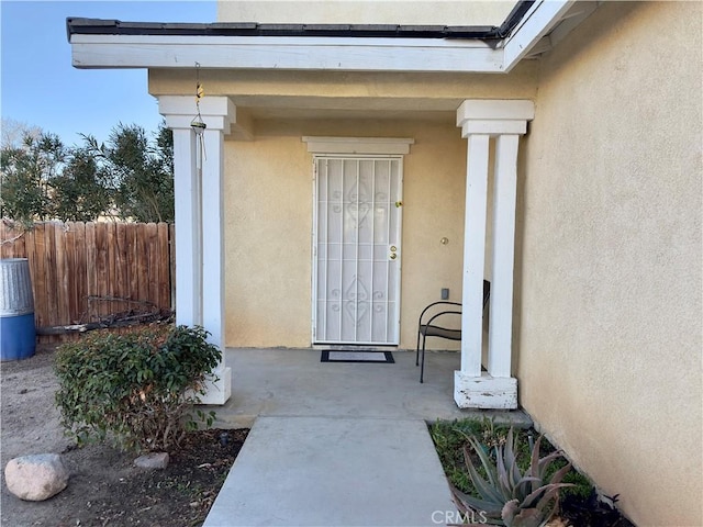 view of exterior entry with fence and stucco siding