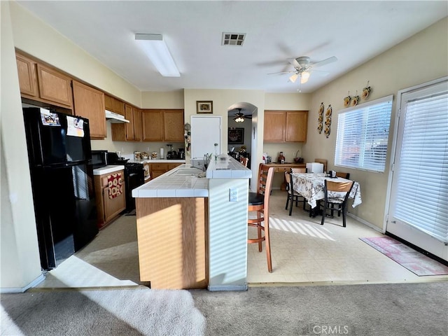 kitchen with brown cabinets, visible vents, tile countertops, and black appliances