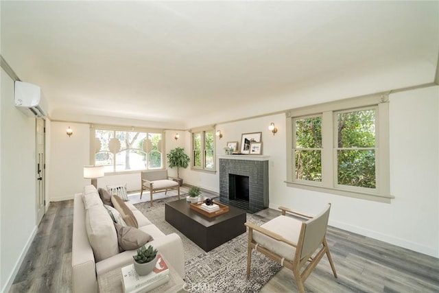 living area featuring a brick fireplace, an AC wall unit, baseboards, and wood finished floors