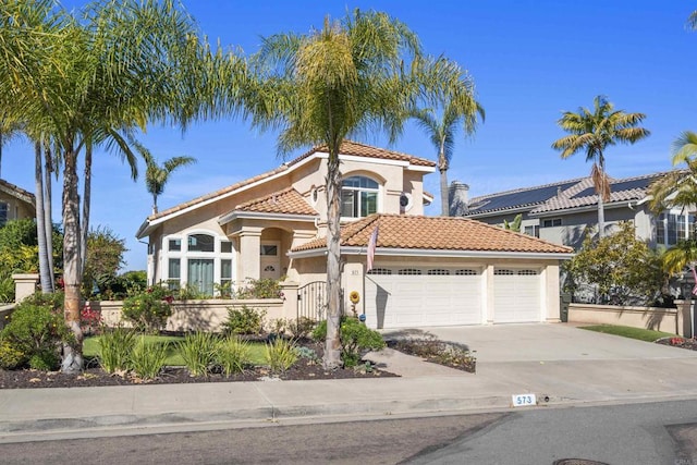 mediterranean / spanish house with a fenced front yard, a tile roof, stucco siding, concrete driveway, and a garage