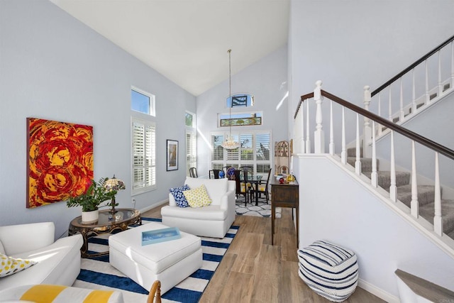 living area featuring light wood-style flooring, high vaulted ceiling, stairway, and baseboards