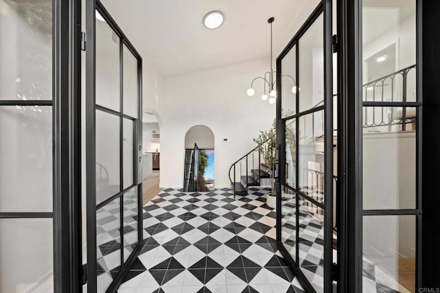 entryway with a wall of windows, arched walkways, a notable chandelier, and a towering ceiling