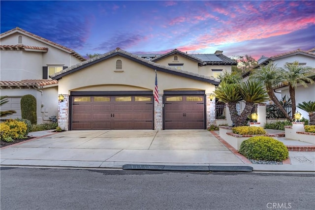 mediterranean / spanish-style house with an attached garage, concrete driveway, stone siding, roof mounted solar panels, and stucco siding