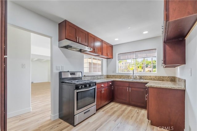 kitchen featuring light wood-style flooring, a sink, gas range, and under cabinet range hood