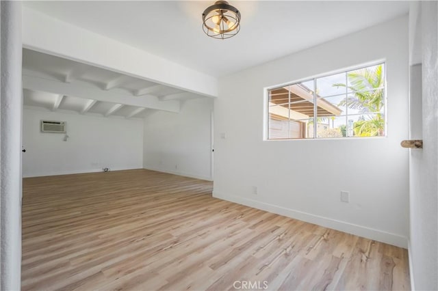 empty room with light wood-style floors, a wall unit AC, vaulted ceiling with beams, and baseboards