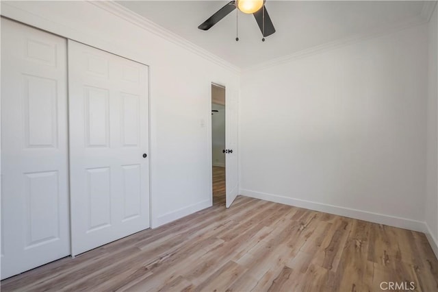 unfurnished bedroom featuring a closet, light wood-style flooring, ornamental molding, a ceiling fan, and baseboards