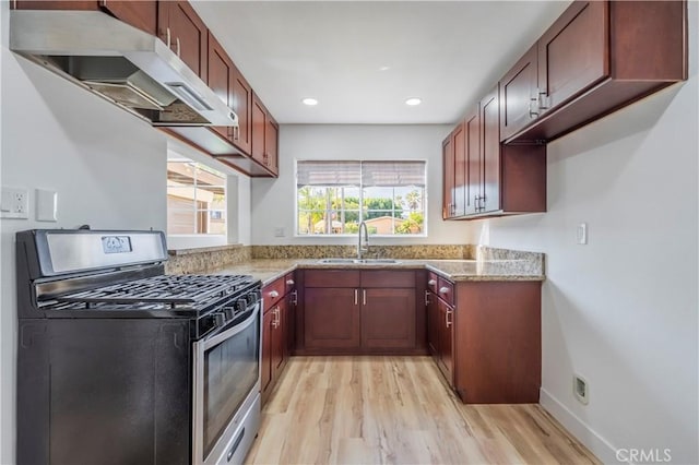 kitchen with light wood finished floors, stainless steel gas range oven, light stone countertops, under cabinet range hood, and a sink