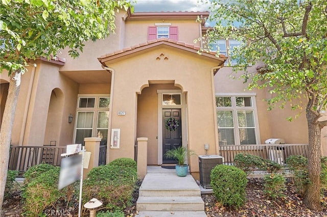 doorway to property featuring central air condition unit, a tile roof, and stucco siding