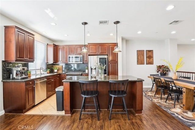 kitchen featuring hanging light fixtures, visible vents, a kitchen island, and appliances with stainless steel finishes