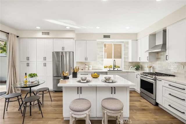 kitchen with visible vents, wall chimney exhaust hood, a kitchen island, appliances with stainless steel finishes, and a sink