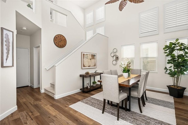 dining space with a high ceiling, ceiling fan, wood finished floors, baseboards, and stairs