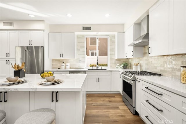 kitchen with wall chimney exhaust hood, visible vents, appliances with stainless steel finishes, and a breakfast bar