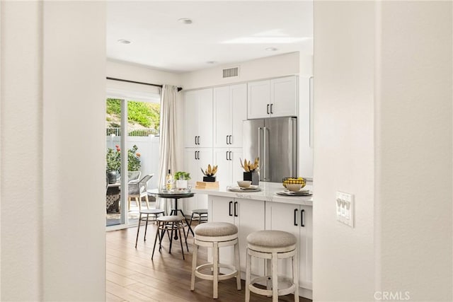 kitchen featuring visible vents, light wood-style floors, white cabinetry, high end fridge, and a kitchen breakfast bar