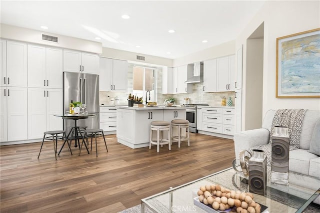 kitchen with stainless steel appliances, a sink, visible vents, white cabinets, and wall chimney range hood