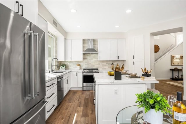 kitchen featuring stainless steel appliances, a kitchen island, a sink, wall chimney range hood, and tasteful backsplash