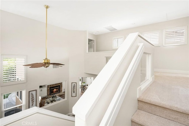 staircase with a fireplace, a high ceiling, a ceiling fan, carpet flooring, and baseboards