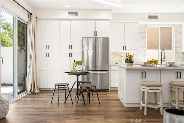 kitchen featuring high end refrigerator, wood finished floors, visible vents, and white cabinetry