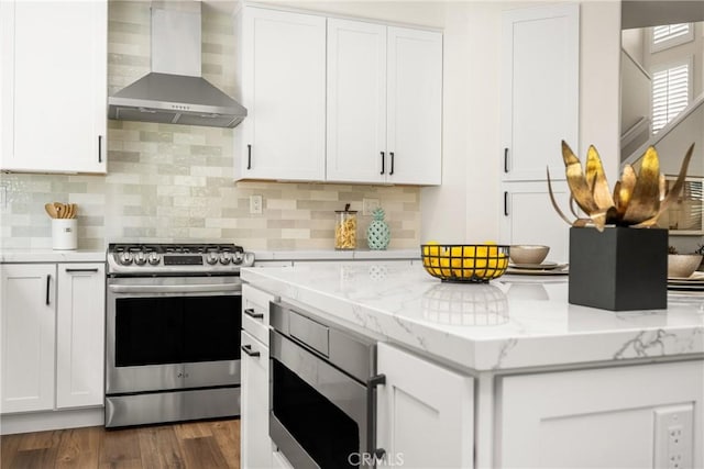 kitchen featuring wall chimney exhaust hood, light stone countertops, white cabinetry, and stainless steel appliances