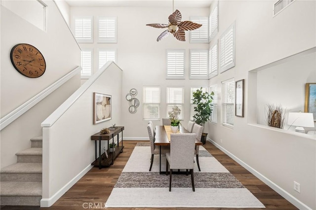 dining room featuring dark wood-style floors, a high ceiling, stairway, and baseboards