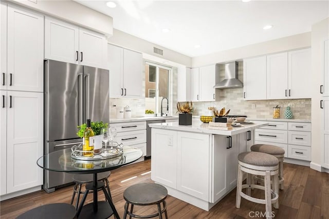 kitchen featuring a breakfast bar area, stainless steel appliances, visible vents, white cabinetry, and wall chimney range hood