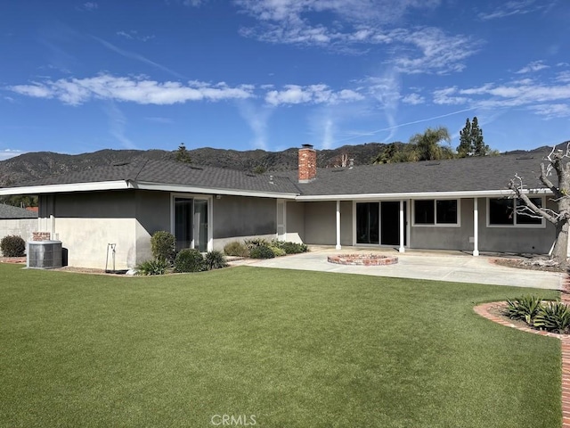 rear view of house featuring central AC, a lawn, stucco siding, a chimney, and a patio area