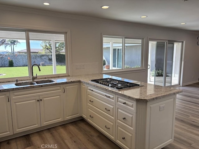 kitchen with light stone counters, stainless steel gas cooktop, a sink, white cabinets, and dark wood-style floors