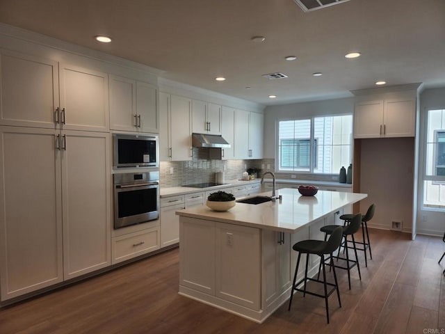 kitchen with a center island with sink, white cabinetry, black electric stovetop, sink, and oven