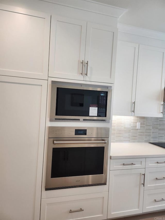 kitchen with black microwave, oven, backsplash, and white cabinets