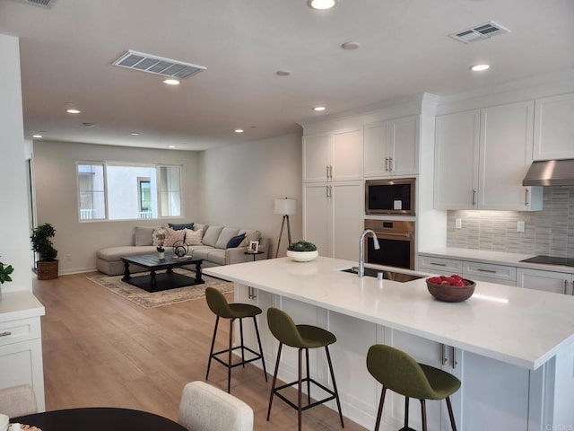 kitchen with sink, a center island with sink, a kitchen bar, and stainless steel oven