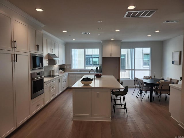 kitchen featuring white cabinets, appliances with stainless steel finishes, a breakfast bar, and a kitchen island with sink