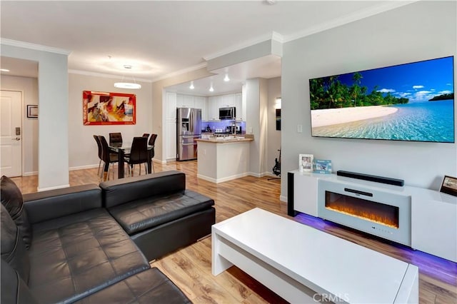 living room featuring light wood finished floors, ornamental molding, a glass covered fireplace, and baseboards