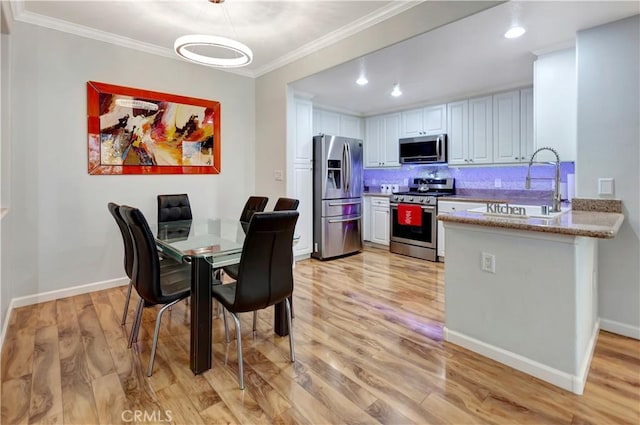 kitchen featuring white cabinets, light wood-style flooring, stainless steel appliances, and crown molding