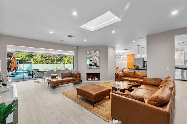 living area with light wood-style flooring, a skylight, visible vents, recessed lighting, and a lit fireplace