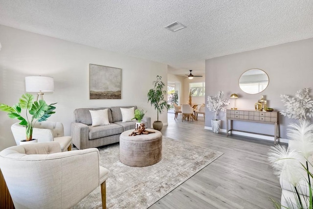 living area with visible vents, a textured ceiling, baseboards, and wood finished floors