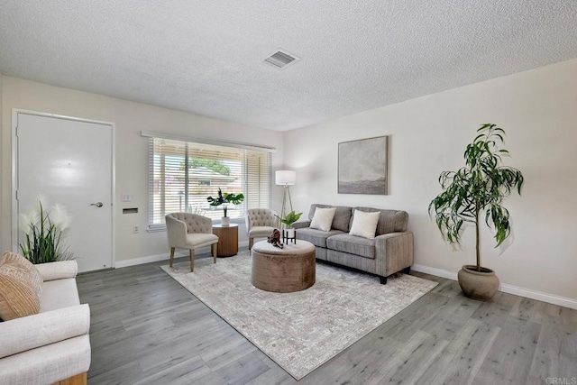 living room with visible vents, a textured ceiling, baseboards, and wood finished floors