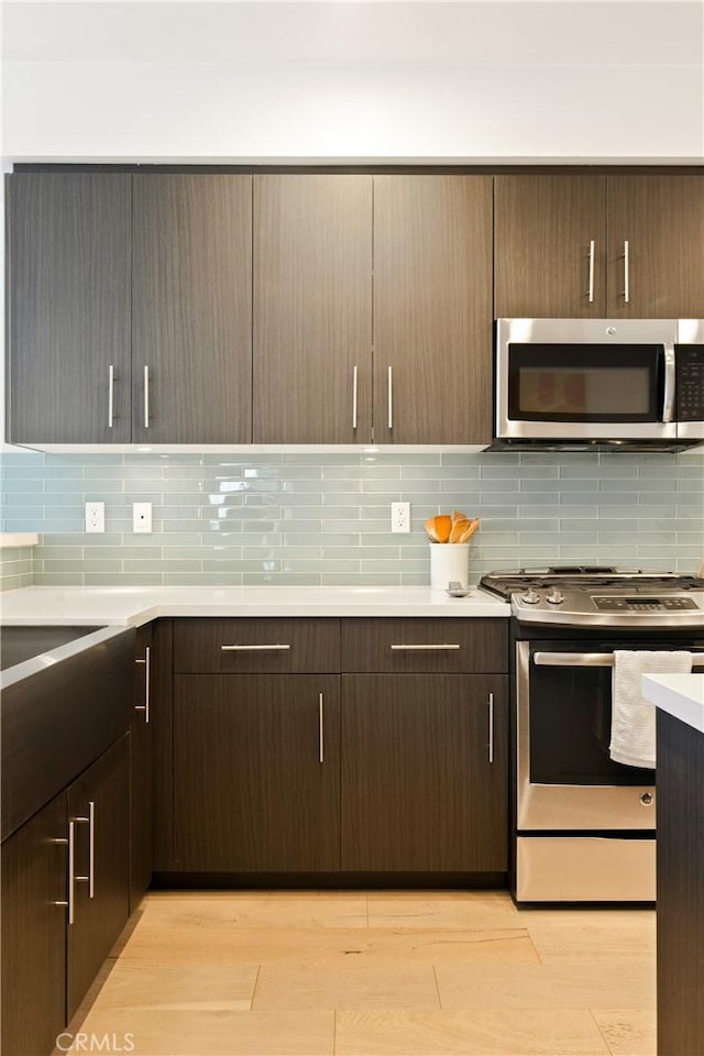 kitchen featuring stainless steel appliances, light countertops, light wood finished floors, and tasteful backsplash