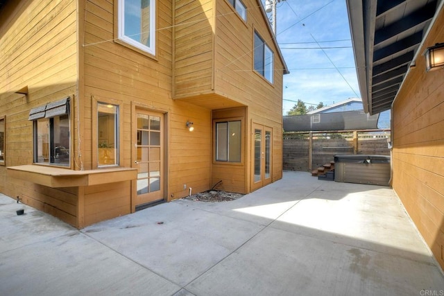 view of side of property featuring a patio, fence, and a hot tub