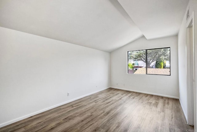 unfurnished room with baseboards, vaulted ceiling, and wood finished floors