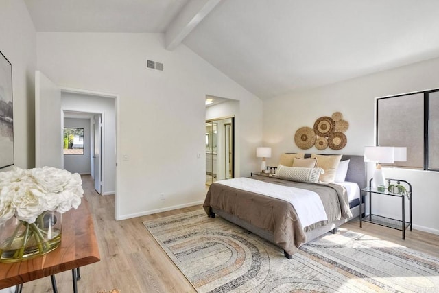 bedroom featuring light wood finished floors, baseboards, visible vents, ensuite bath, and beam ceiling