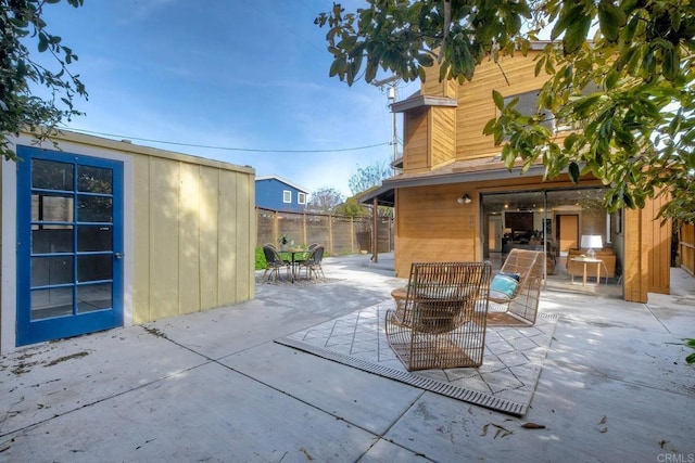 view of patio with outdoor dining space, fence, and an outbuilding