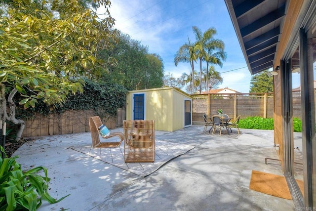 view of patio / terrace with an outbuilding, a shed, outdoor dining space, and a fenced backyard