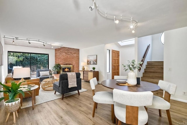 dining room with a skylight, stairway, light wood-type flooring, a fireplace, and track lighting