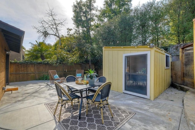 view of patio / terrace featuring a storage shed, a fenced backyard, outdoor dining area, and an outbuilding